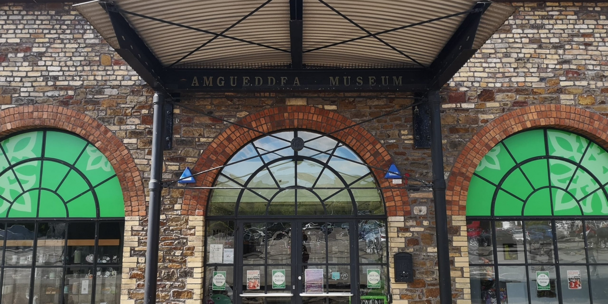 Front of industrial looking build entrance under shelter centre flanked by one brick arch on either side