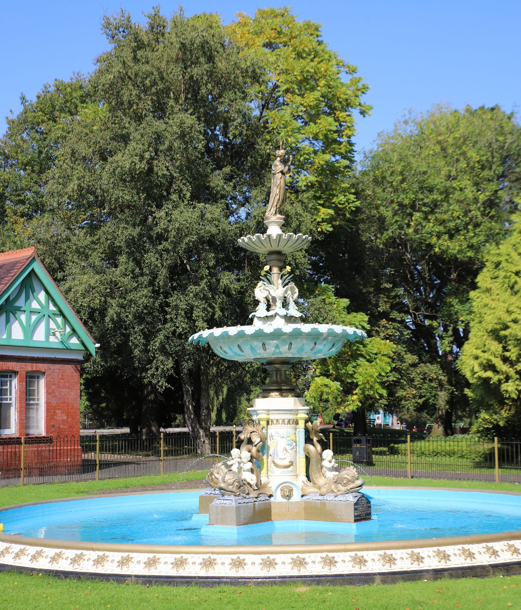 Fountain in park land with trees behind and clear blue sky above
